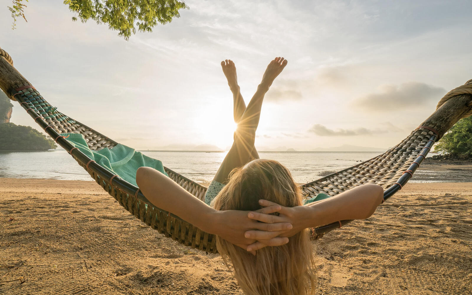 A female professional holding a yellow coffee mug while working on her laptop on the patio of a cabin, surrounded by nature.